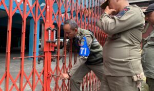Petugas Satpol PP sedang mencoba merusak paksa gembok gedung Perbasi yang masih dikunci oleh pihak pengelola. (Foto: Indri)